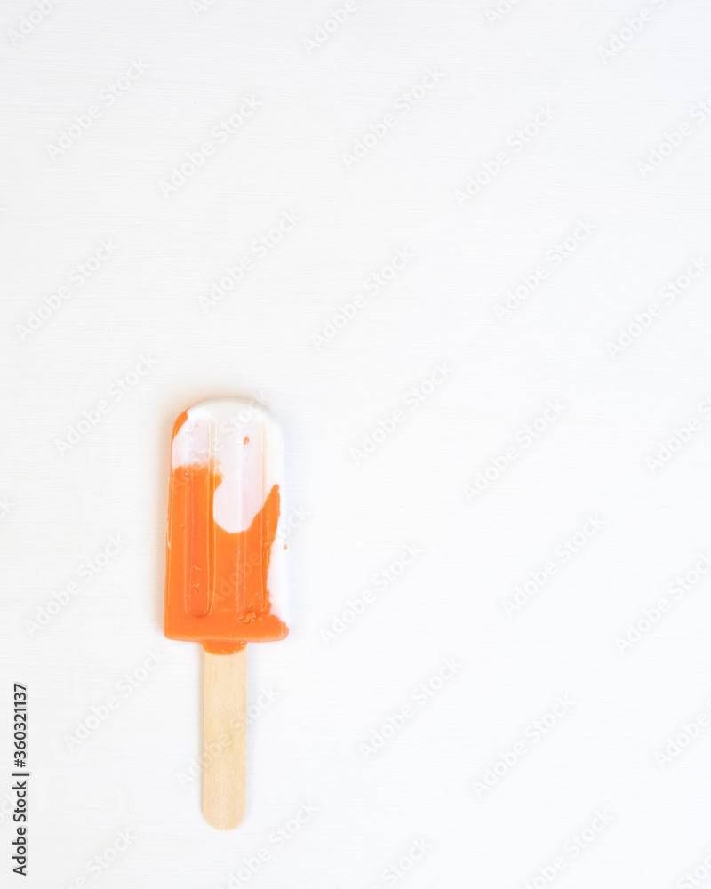 Orange and white creamsicle on a stick in a vertical photo with a white background. Orange and white creamsicle on a stick in a vertical photo with a white background.
