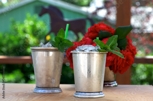 Mint julep drinks in silver cups with red roses and horse silhouette in background