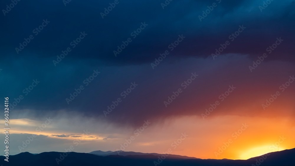 Beautiful bright sunset sky over the mountains silhouette . Dramatic orange clouds after sunset. Nature backgrounds. Golden sunset.
