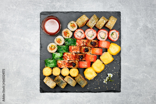 Fresh fish sushi set with side dishes on a black graphite board and gray background