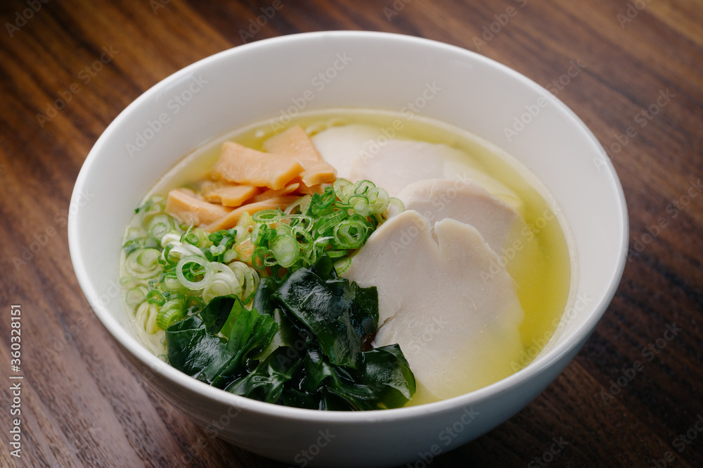chicken broth ramen noodle soup with poached chicken breast, bamboo shoots, seaweed, scallion in a white bowl on wooden table chicken broth ramen noodle soup with poached chicken breast, bamboo shoots, seaweed, scallion in a white bowl on wooden table