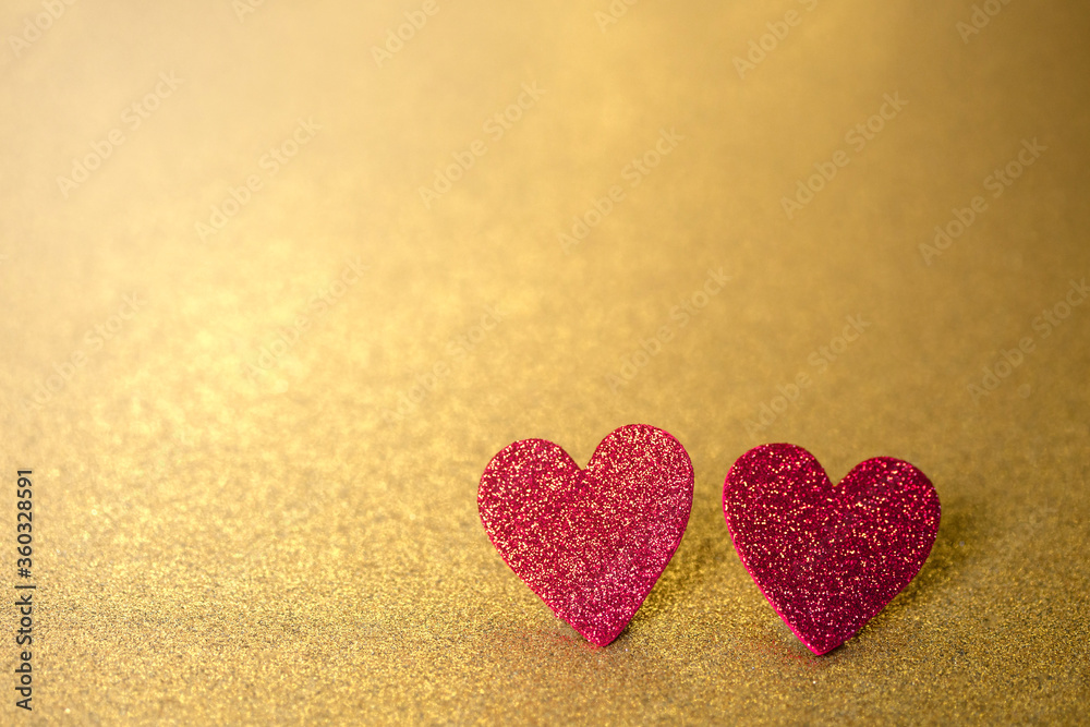Two red hearts like a couple on a gold glitter and sequin background that sparkles and has lots of copy space