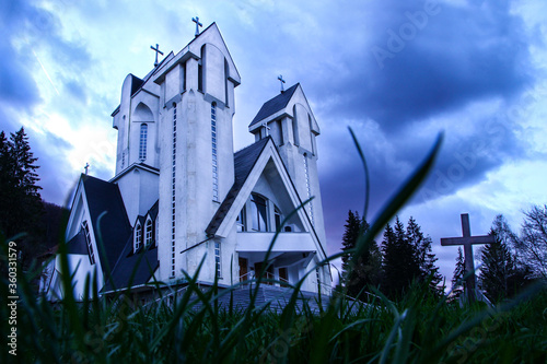 Spooky graveyard with church in the background. A cross is seen against the dark sky.