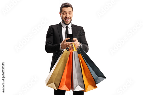 Excited businessman with shopping bags typing on a mobile phone