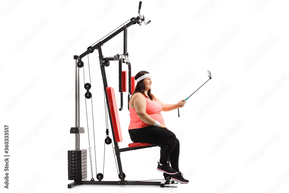 Corpulent woman sitting on a fitness machine and taking a selfie with a stick Corpulent woman sitting on a fitness machine and taking a selfie with a stick