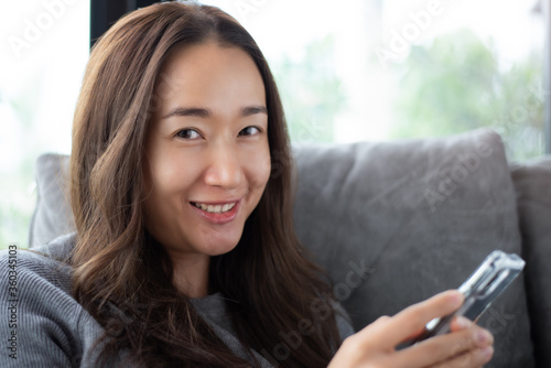Portrait of smiling Asia woman looking at camera and using smart phone. Happy message concept.