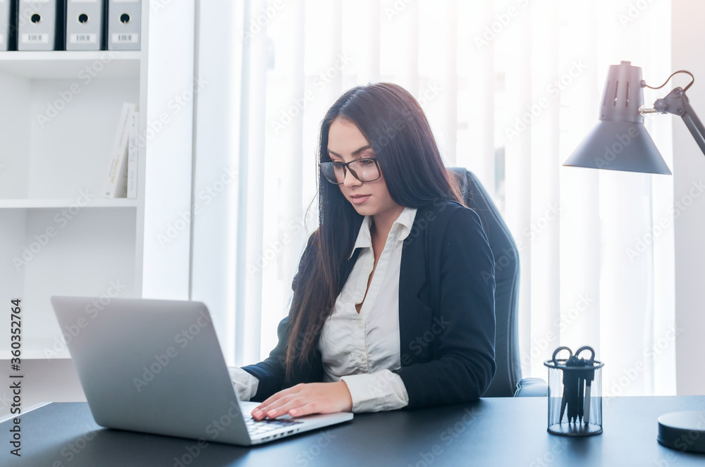 Young cheerful girl sitting in her bright office while looking at the laptop. Young cheerful girl sitting in her bright office while looking at the laptop.