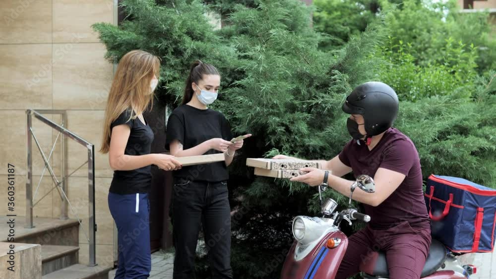 Two girls pick up delivery food box from delivery rider with scooter in front house for social distancing for infection risk