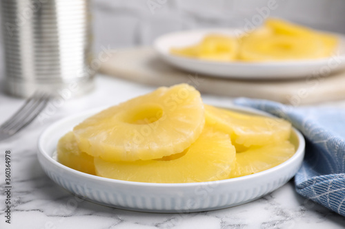 Fotografie Tasty canned pineapple slices on white marble table, closeup