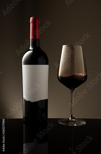 A bottle and a glass of red wine with swirl and waves inside the glass on a beige background