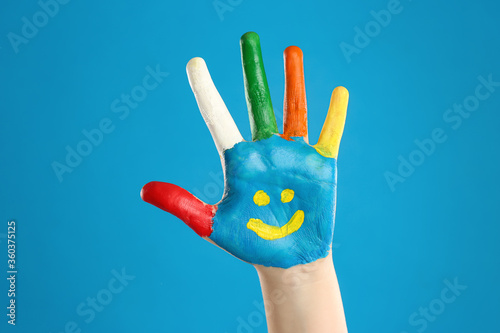 Kid with smiling face drawn on palm against blue background  closeup
