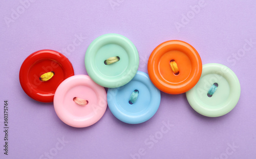 Many colorful sewing buttons on violet background, flat lay