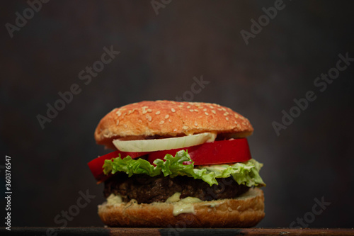 primer plano de hamburguesa con lechuga tomate cebolla carne picada sobre madera con fondo oscuro