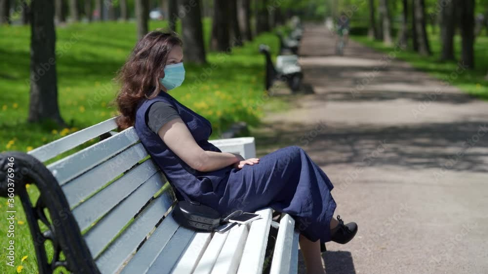 Woman wearing protective medical face mask for covid-19 epidemic, woman with mask on bench in park, coronavirus pandemic flu corona virus, human face masked for 2019-ncov. Woman wearing protective medical face mask for covid-19 epidemic, woman with mask on bench in park, coronavirus pandemic flu corona virus, human face masked for 2019-ncov.