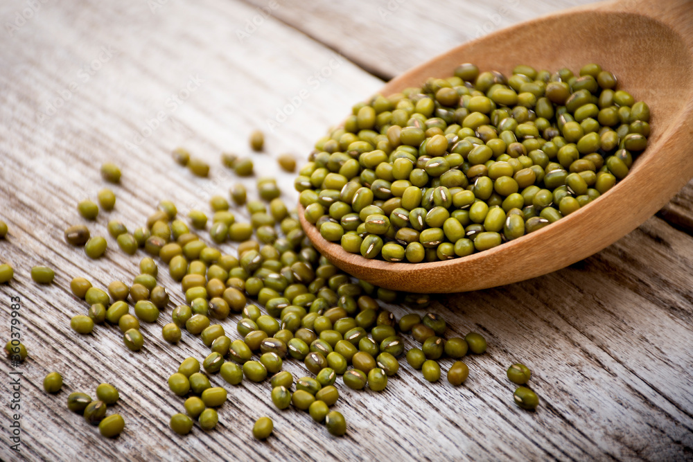 Green mung beans in wooden spoon isolated on wood table background. Selective focus. Green mung beans in wooden spoon isolated on wood table background. Selective focus.