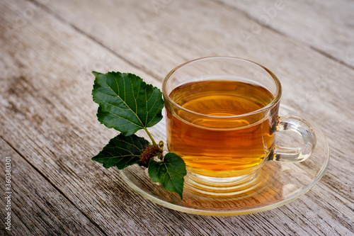 Glass cup of hot mulberry leaf tea on rustic wood table background. Healthy drinks concept. 