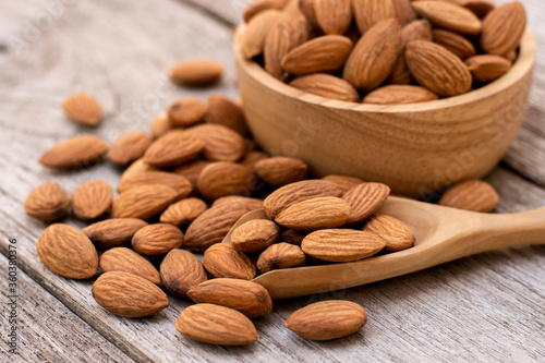 Closeup almond nuts in wooden bowl and scoop isolated on rustic wood table  background. 