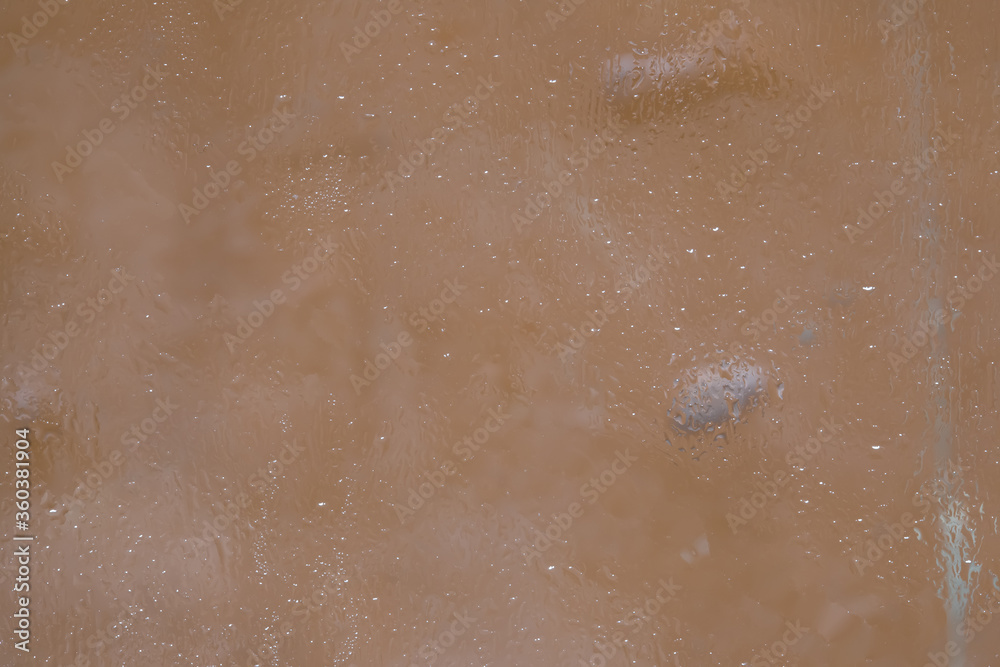 Fototapeta premium A fragment of a glass surface covered with a thin layer of melting ice is located on the background of the color of coffee with milk. Soft focus.