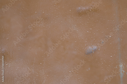 A fragment of a glass surface covered with a thin layer of melting ice is located on the background of the color of coffee with milk. Soft focus.