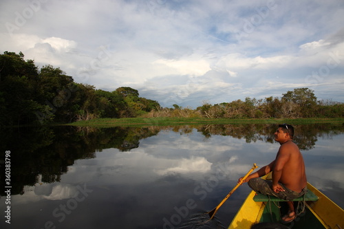 Shirtless man with paddle sitting on a fishing boat at sunset in Amazon jungle river, Brazil