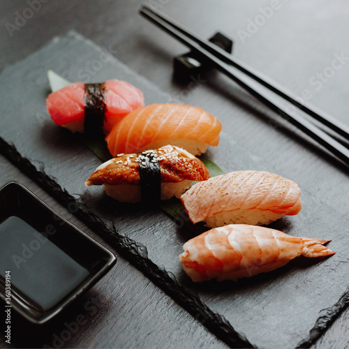 Sashimi sushi. A set of nigiri sushi on a black slate tray with soy sauce and chopsticks on a stand.