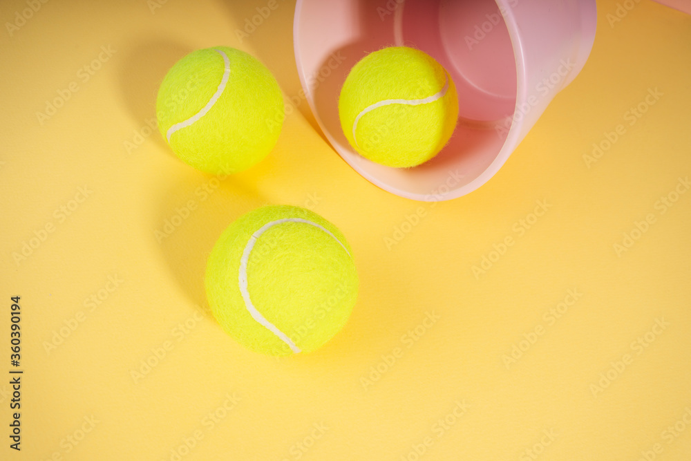 Three tennis balls and pink basket on orange yellow background.