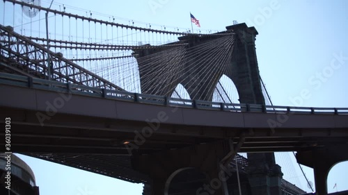 Brooklyn Bridge view from below in New York City with USA flag waving in slow motion