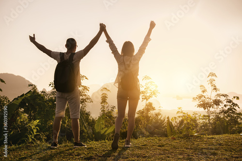 Two happy tourists with raised arms at sunrise