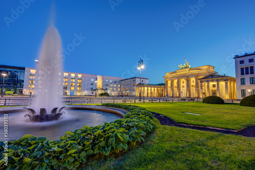 The illuminated Brandenburg Gate in Berlin at dusk with a fountain