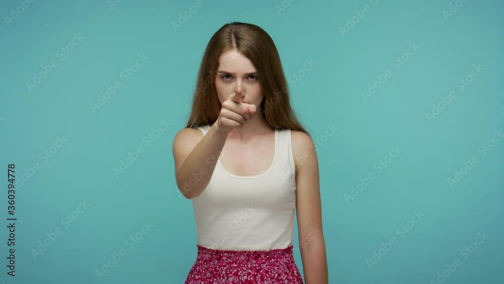 Hey you! Serious dissatisfied girl pointing finger to camera, looking strict angry and choosing guilty, noticing something suspicious, accusing for mistake. studio shot isolated on blue background Hey you! Serious dissatisfied girl pointing finger to camera, looking strict angry and choosing guilty, noticing something suspicious, accusing for mistake. studio shot isolated on blue background