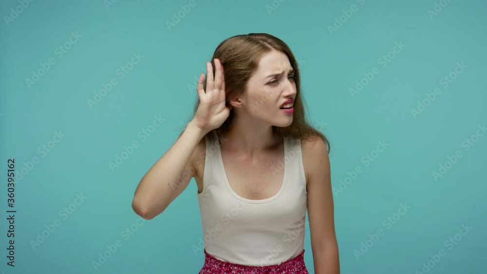 What? I can't hear you! Confused girl having hearing problems, asking to say louder, difficult to listen quiet talk, misunderstanding in communication. indoor studio shot isolated on blue background What? I can't hear you! Confused girl having hearing problems, asking to say louder, difficult to listen quiet talk, misunderstanding in communication. indoor studio shot isolated on blue background