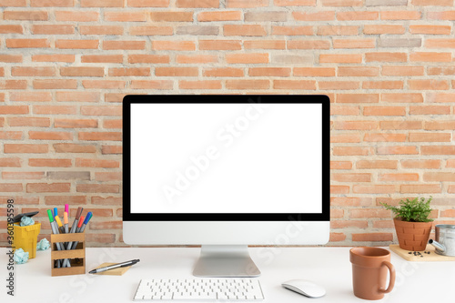 Display Computer desktop with mock-up white screen on white table have colourful magic pen and brown coffee cup including lovely ornamental in clay pots with brick wall background in home office.