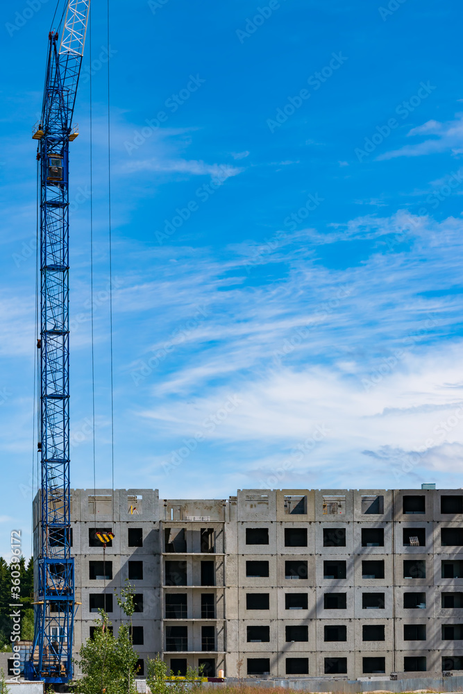 A crane over a house under construction against the blue sky