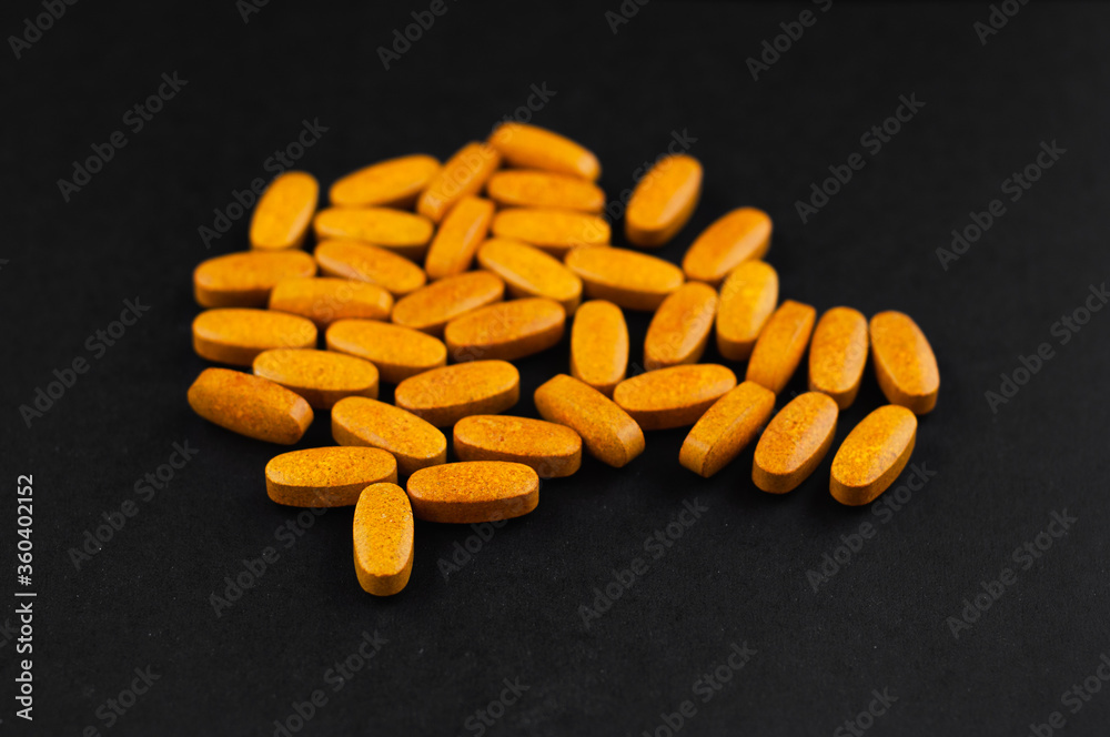 Bright yellow oblong tablets in the form of capsules on a black background Bright yellow oblong tablets in the form of capsules on a black background