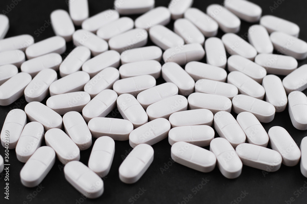 White oblong tablets in the form of capsules on a black background White oblong tablets in the form of capsules on a black background