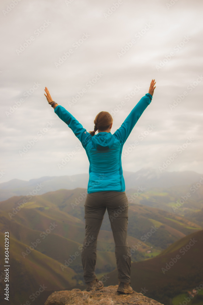 Unknown girl from back standing on top of mountains unfocused. Blurred photo of pilgrim with hands up in Pyrenees mountains. Camino de Santiago background. Freedom and success concept. Active people. Unknown girl from back standing on top of mountains unfocused. Blurred photo of pilgrim with hands up in Pyrenees mountains. Camino de Santiago background. Freedom and success concept. Active people.