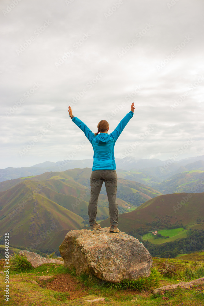Unknown girl from the back standing on top of mountains. Pilgrim with hands up in Pyrenees mountains, France. Camino de Santiago background. Freedom and success concept. Active people concept. Unknown girl from the back standing on top of mountains. Pilgrim with hands up in Pyrenees mountains, France. Camino de Santiago background. Freedom and success concept. Active people concept.