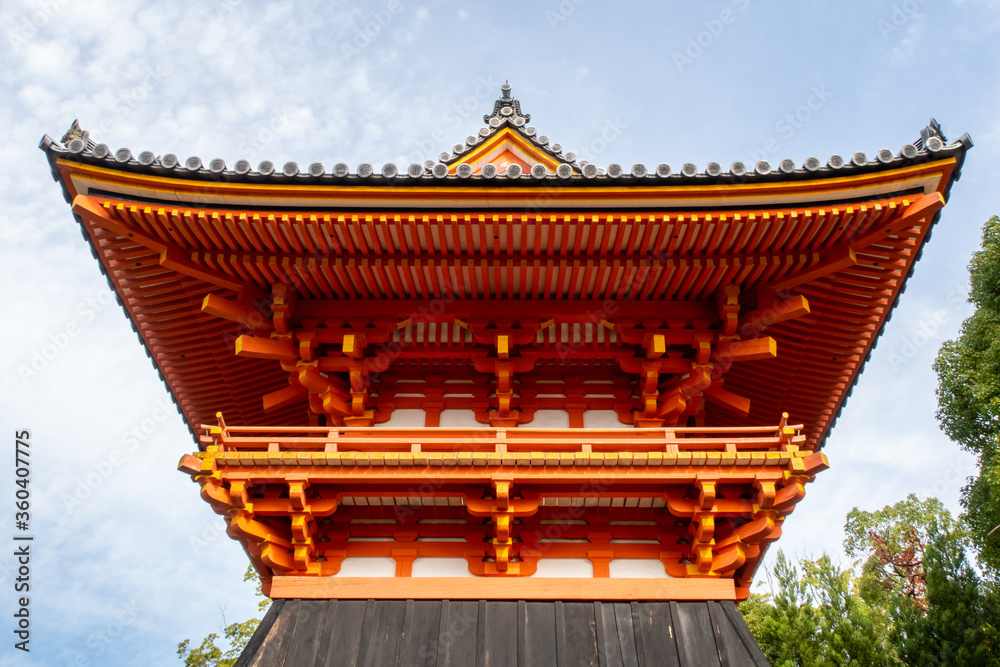 Naklejka premium Symmetrical front view of traditional orange wooden Syoro Pagoda with carved roof in Ninna-ij Temple in Kyoto, Japan, with blue sky in the background, autumn.