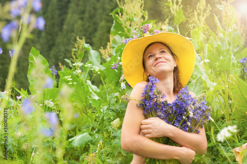 Beautiful happy young girl in yellow hat with purple flowers smiling in the green mountains