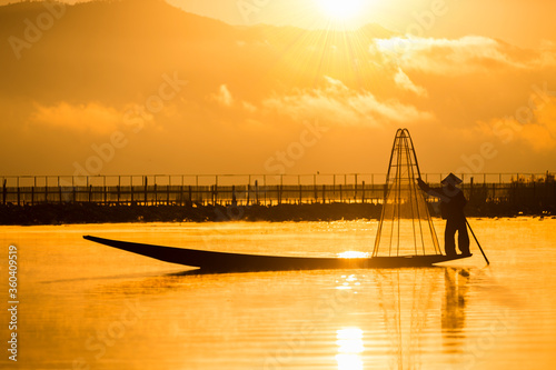 A fisherman show catches fish for food in sunrise rays at Inle lake ,Myanmar .Intha people lifestyle with blue white cloud sun sky photo