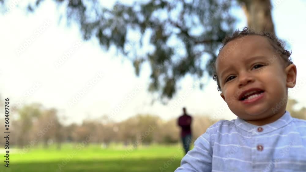 Little African American boy walking on lawn, holding red apple, biting and eating it. His father watching son out-of-focus. Family and weekend concept Little African American boy walking on lawn, holding red apple, biting and eating it. His father watching son out-of-focus. Family and weekend concept