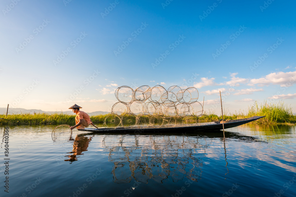 Obraz premium A fisherman show catches fish for food in sunrise rays at Inle lake ,Myanmar .Intha people lifestyle with blue white cloud sun sky
