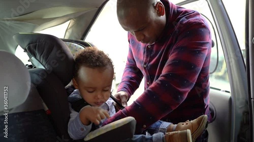 African American bald dad checking belts on child car seat. Focused young father protecting in case of emergency. Safety and transportation concept