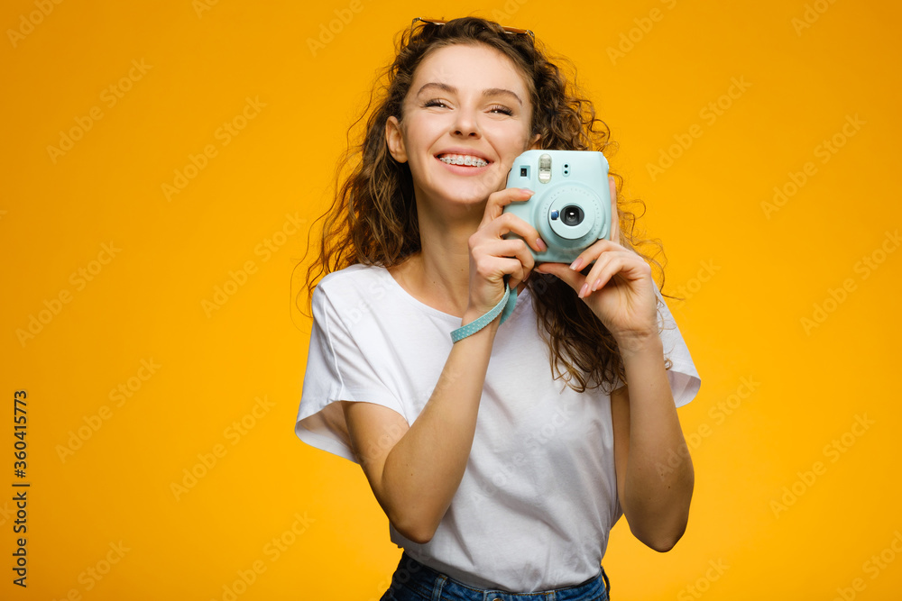 Fototapeta premium Beautiful girl with camera isolated on yellow background