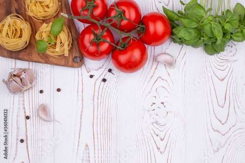 Top view raw tagliatelle pasta with fresh basil, garlic and tomatoes on a rustic white table, flat lay, copy space.