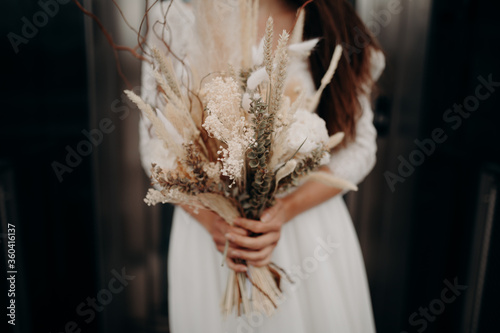 a bride posing outdoors with her bouquet of dried flowers in her hand