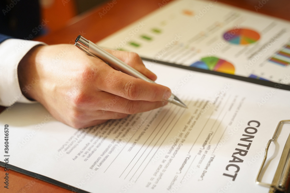 Businessman sitting at office desk signing a contract with shallow focus on signature. Businessman sitting at office desk signing a contract with shallow focus on signature.