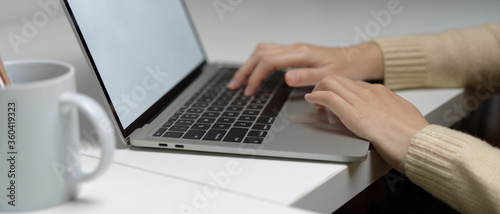 Female worker typing on mock-up laptop with coffee mug on white worktable