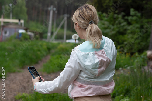 girl is blows away dandelion blowball and doing selfi on phone