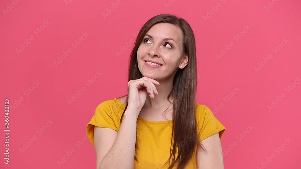Dreamful happy charming beautiful brunette young woman in yellow t-shirt posing isolated on pink background studio. People sincere emotions lifestyle concept. Looking at camera with smile think dream Dreamful happy charming beautiful brunette young woman in yellow t-shirt posing isolated on pink background studio. People sincere emotions lifestyle concept. Looking at camera with smile think dream